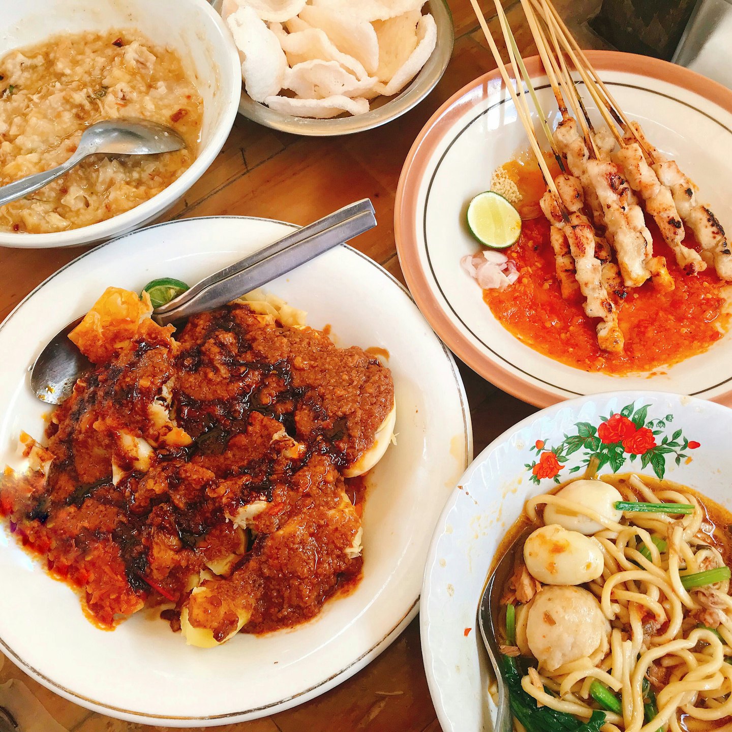 Asian dishes including porridge, satay, and noodles on a wooden table.