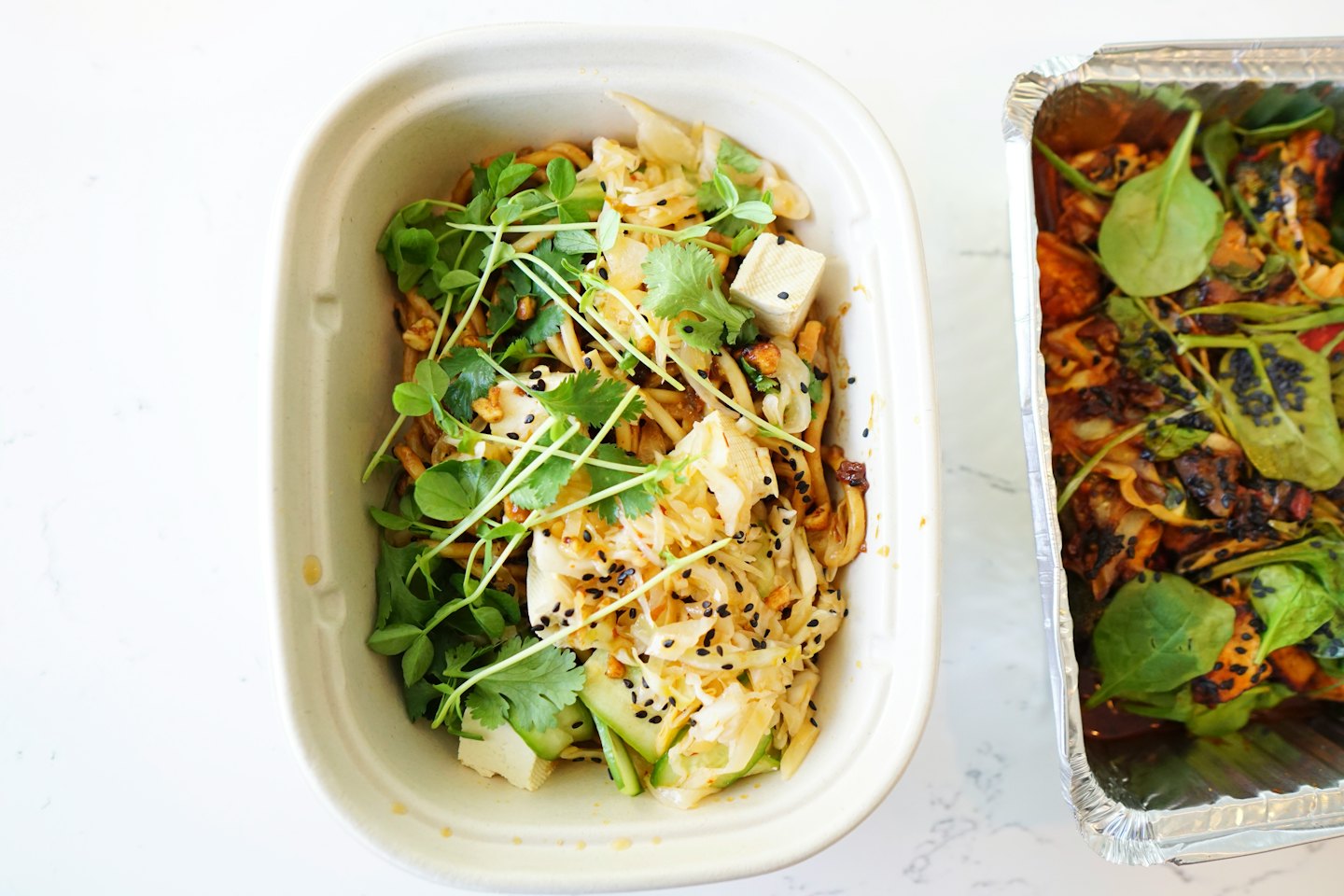 Two take-out containers filled with fresh noodle and vegetable dishes.