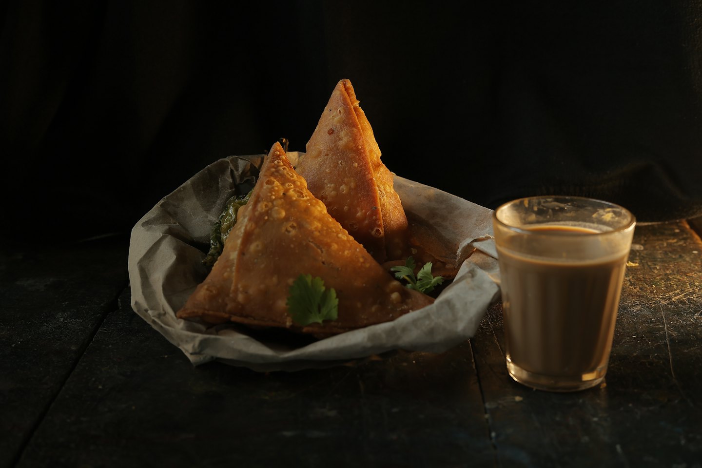 Golden samosas and chai served in a basket on a wooden table.