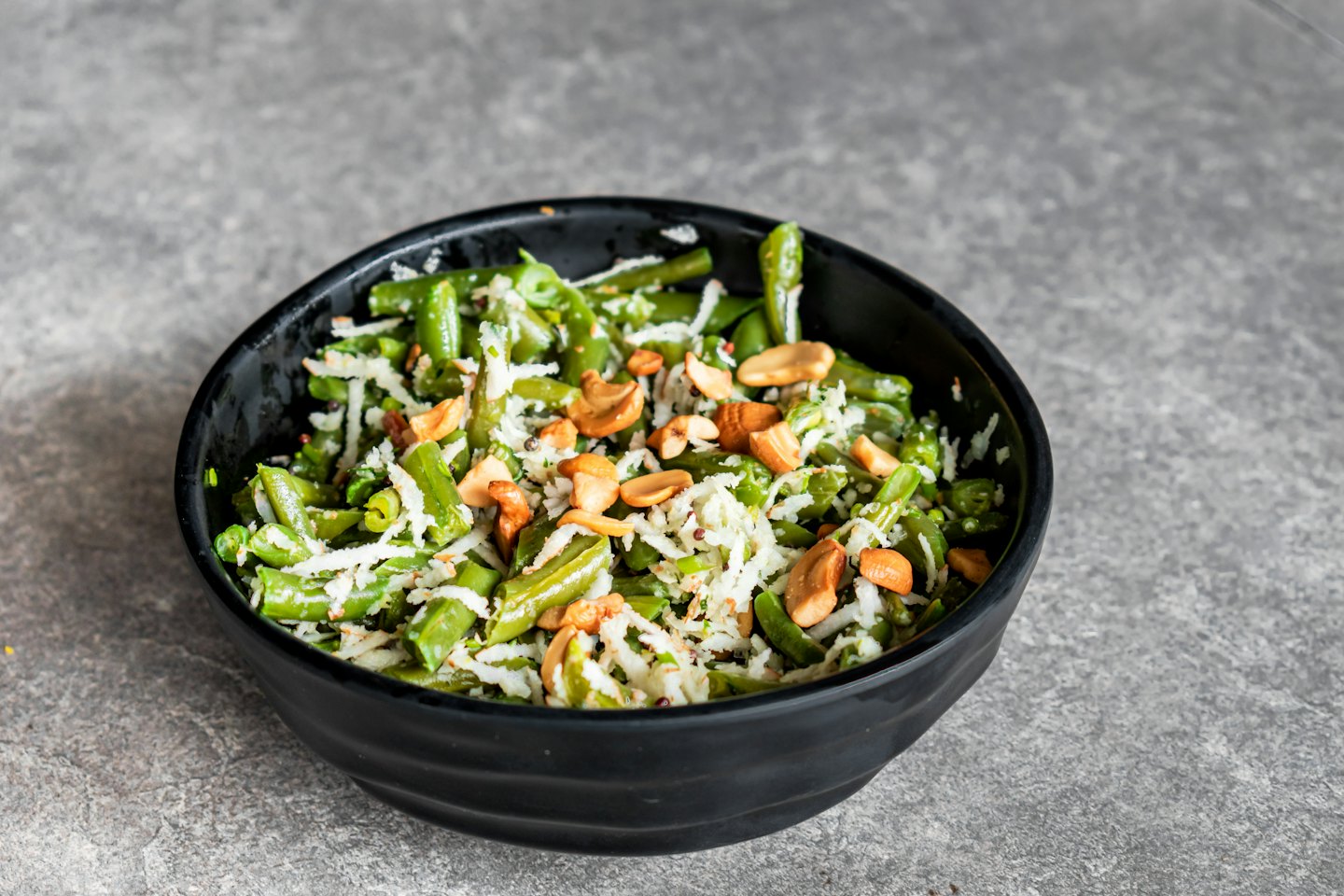 Black bowl of green bean salad with coconut and nuts.