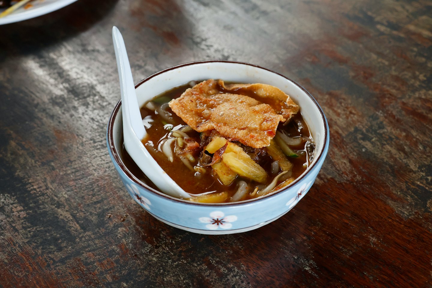 A bowl of Laksa noodle soup sits on a wooden table.