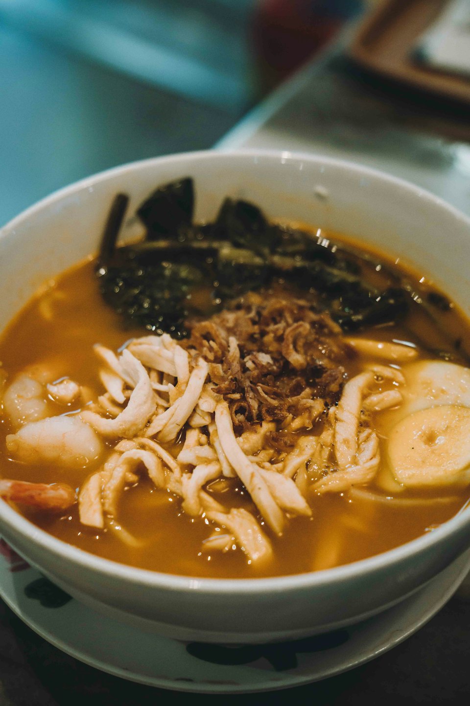 Steaming bowl of chicken noodle soup with shrimp and egg.
