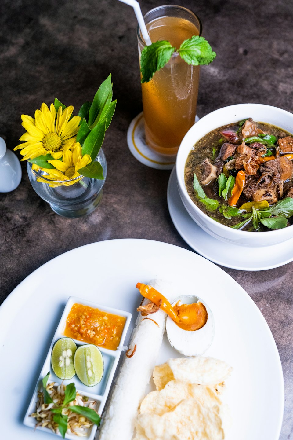Southeast Asian feast laid out on a dark table with iced tea.
