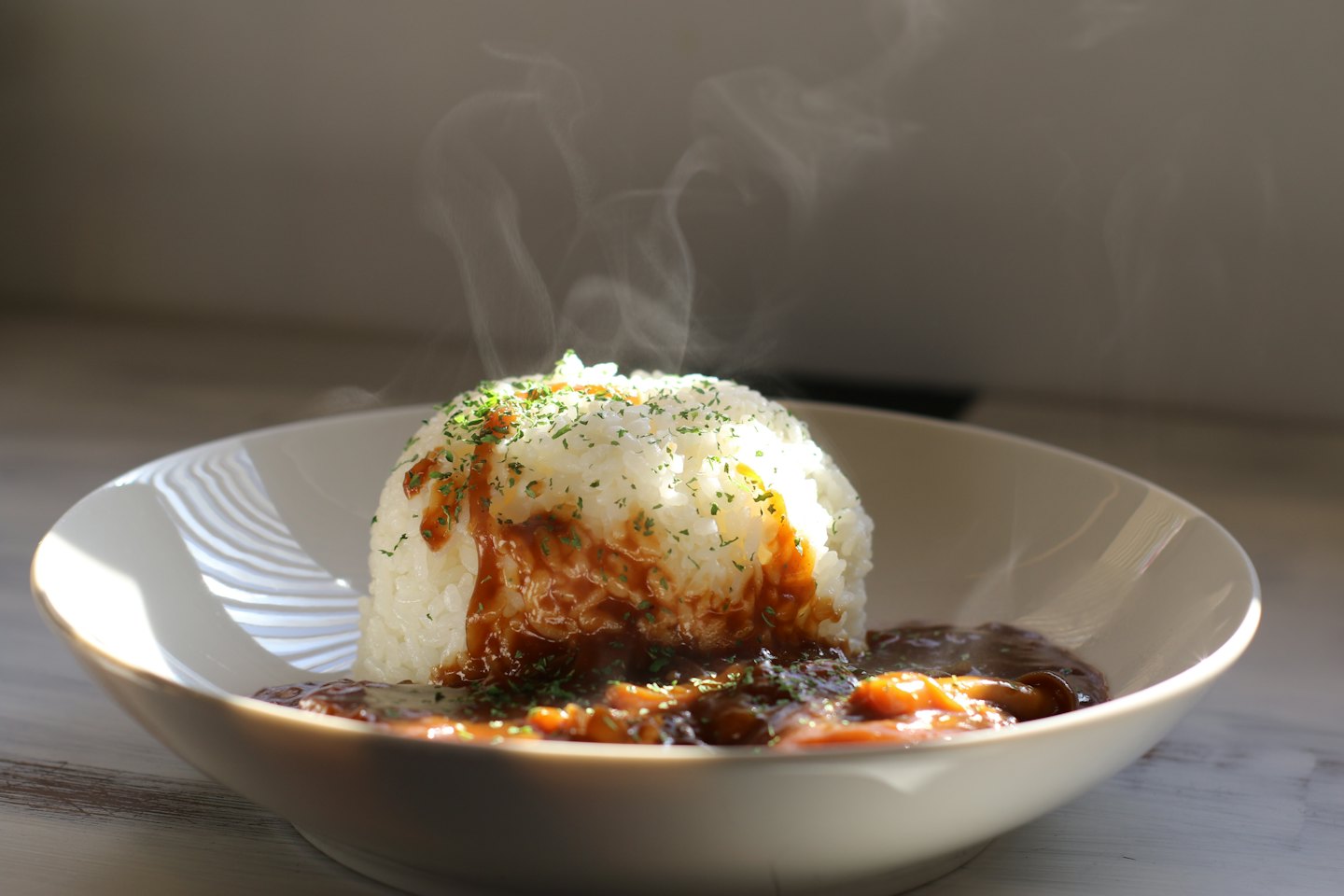 Steaming bowl of mushroom curry over rice on wooden table.