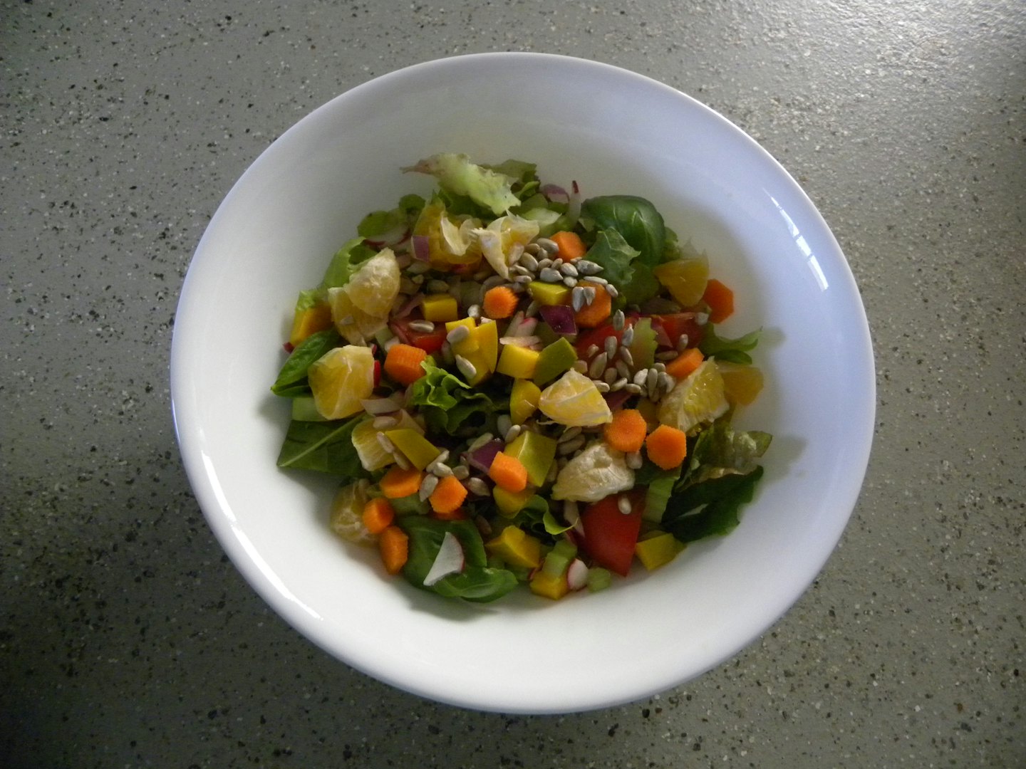 A bowl of colorful salad sits on a speckled countertop.