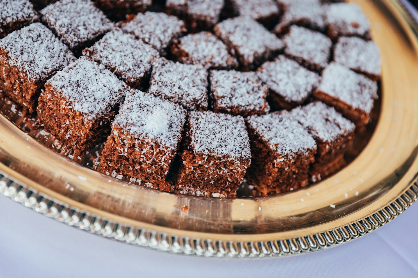 Square chocolate cakes topped with coconut on a golden platter.