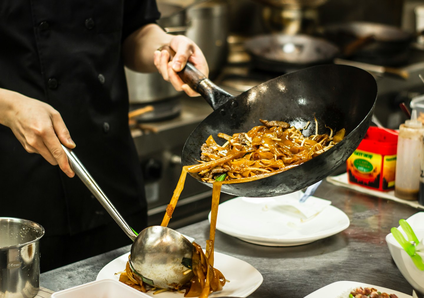 Chef plating stir-fried noodles with beef onto a white plate.